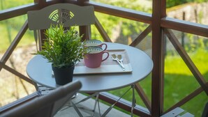 Una pequeña mesa redonda con una planta en maceta, tazas rosas y una cuchara en un balcón con barandas de madera.
