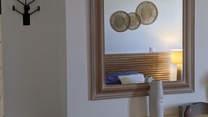 Un dormitorio con un espejo grande, una cama con almohada azul y una mesita de noche con lámpara.