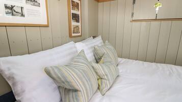 Una cama con ropa blanca y almohadas estampadas, un panel informativo enmarcado y un techo de madera.