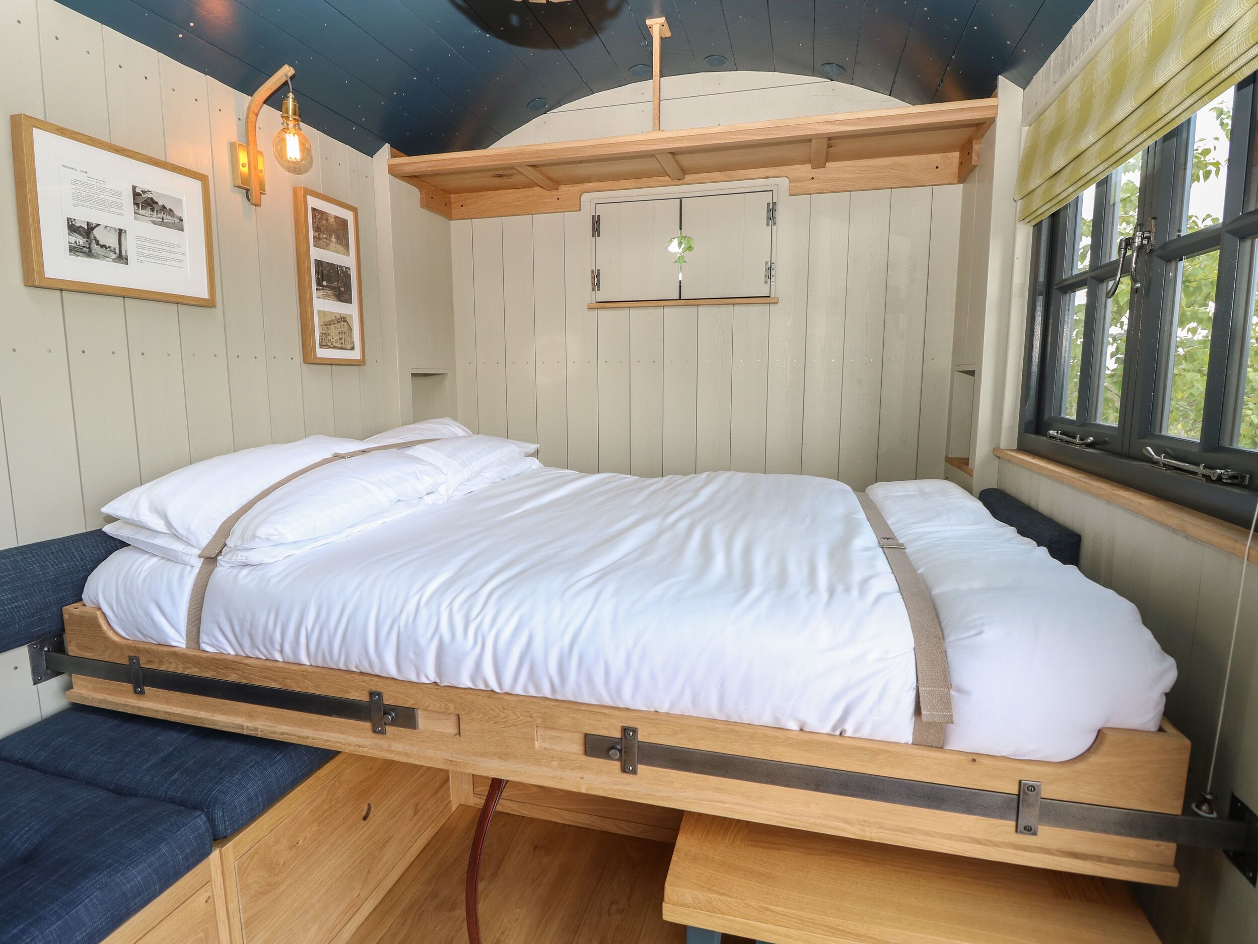 Una cama con estructura de madera y ropa de cama blanca en una habitación con paredes y techo inclinados de madera.