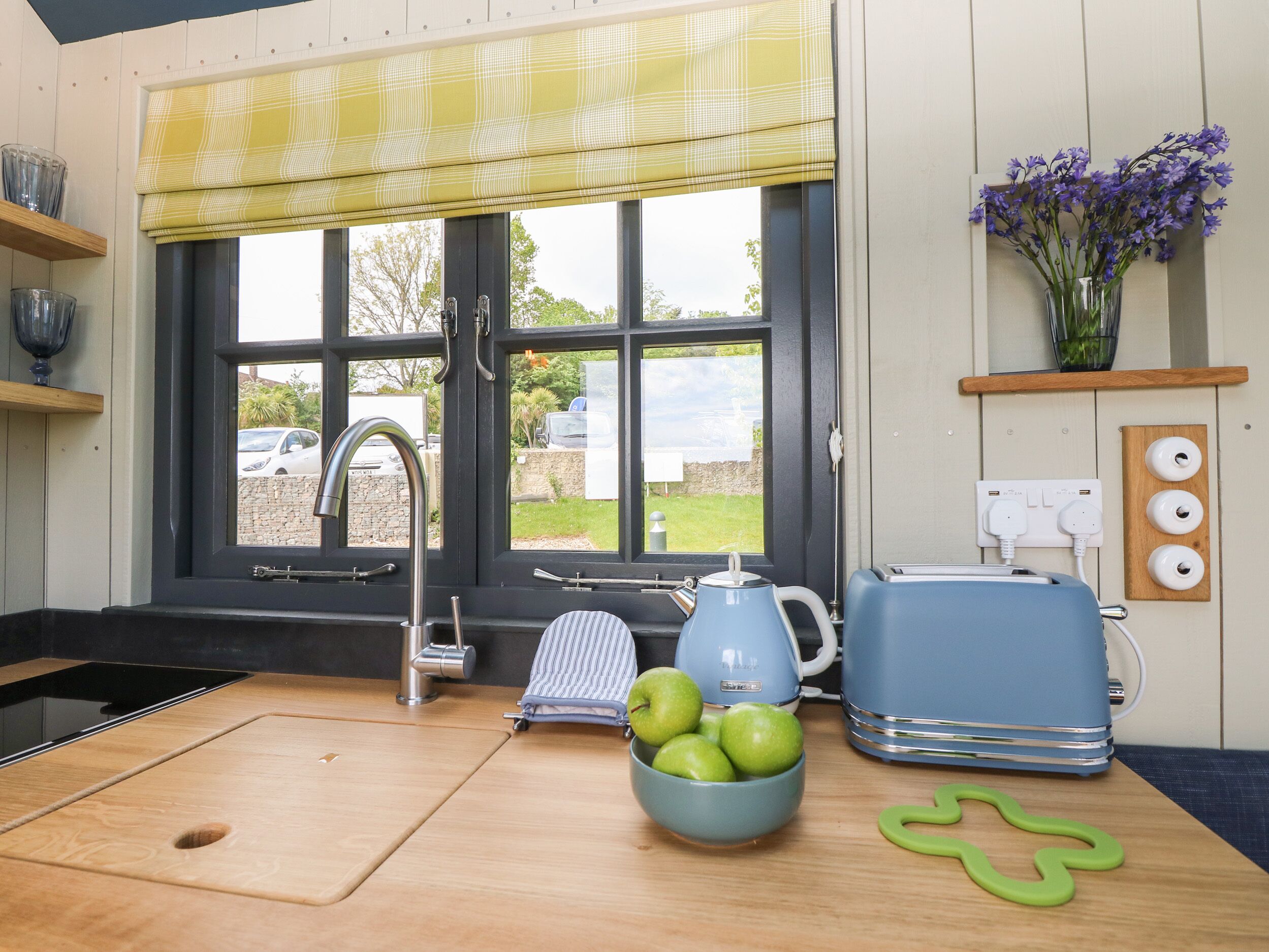 A kitchen with a window, a sink, a kettle, a toaster, and a bowl of apples.