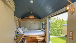 A compact, well-lit bedroom with a bed, wooden furniture, and a view of a green garden. - Malbec (Ryde)