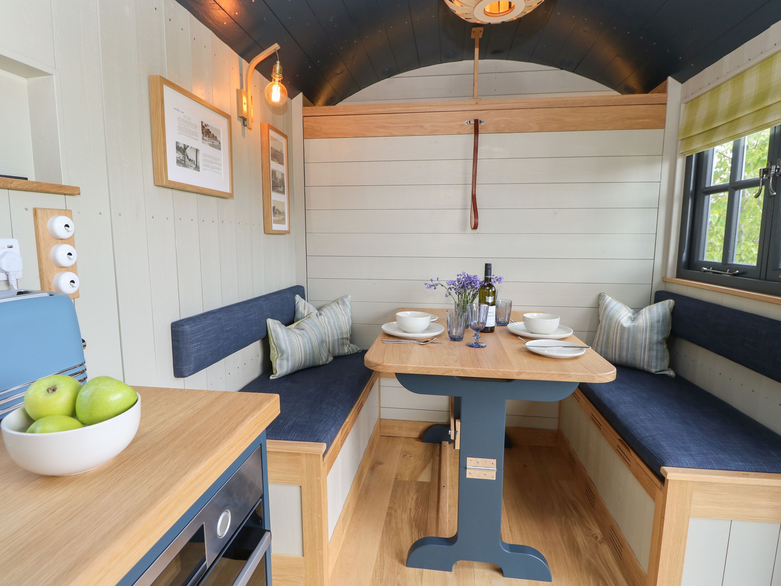 A cozy dining area with a wooden table, blue cushioned seating, and a bowl of green apples.