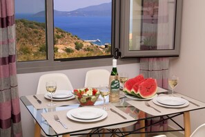 Enjoy a romantic meal with a view of the sea and mountains from this dining area, featuring a table set for two.