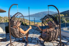 Relax in a comfortable, elevated swing chair, suspended above a stone-tiled patio with a serene lake view.