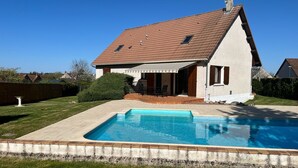 Una casa con piscina, un porche cubierto y un césped bien cuidado.
