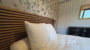 Una cama con cabecera de madera, almohadas blancas y una colcha texturizada de color blanco.