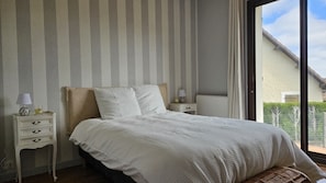 Un dormitorio con cama, mesita de noche, lámpara y vistas al exterior.