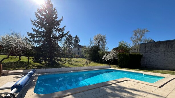 Una piscina rectangular con superficie de agua azul transparente, rodeada por un solárium de baldosas.