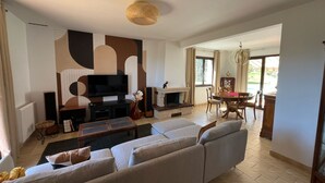 Una sala de estar moderna con un sofá grande, un televisor de pantalla plana, una chimenea y un comedor con mesa y sillas.