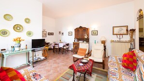 A living room with a sofa, TV, dining table, and chairs. There are decorative plates on the wall and a cabinet with a mirror. - 3363 Casa Giovanna by Barbarhouse (Ischitella)