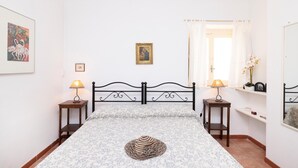A bedroom with a bed, two bedside tables, a lamp, a framed picture, a window with curtains, and a mirror. - 3363 Casa Giovanna by Barbarhouse (Ischitella)