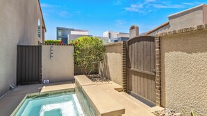 A swimming pool area with a gated entrance, a small garden, and a view of neighboring buildings.