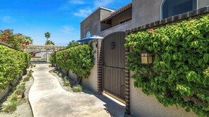 A pathway leading to a gated entrance with a building featuring a large arched window and a covered patio area.