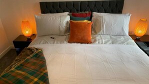 A neatly made bed with white linens, a black tufted headboard, and multiple pillows in various colors. - Immaculate 2-bed Apartment in Grays (Grays)