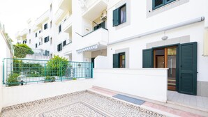 A courtyard with a patterned floor, a green metal fence, and a white building with balconies and a door. - 3362 Raggio di Sole by Barbarhouse (Vieste)