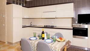 A modern kitchen with white cabinets, a gas stove, an oven, and a dining table set with plates, glasses, and a bottle. - 3362 Raggio di Sole by Barbarhouse (Vieste)