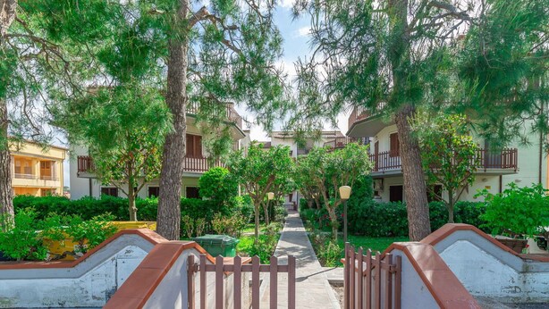 A pathway leading to a row of buildings with balconies, surrounded by trees and greenery. - Italian Experience - Conero Garden Apt (Marcelli)