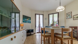 A dining area with a wooden table and chairs, a chandelier, and a view through the glass door. - Italian Experience - Conero Garden Apt (Marcelli)