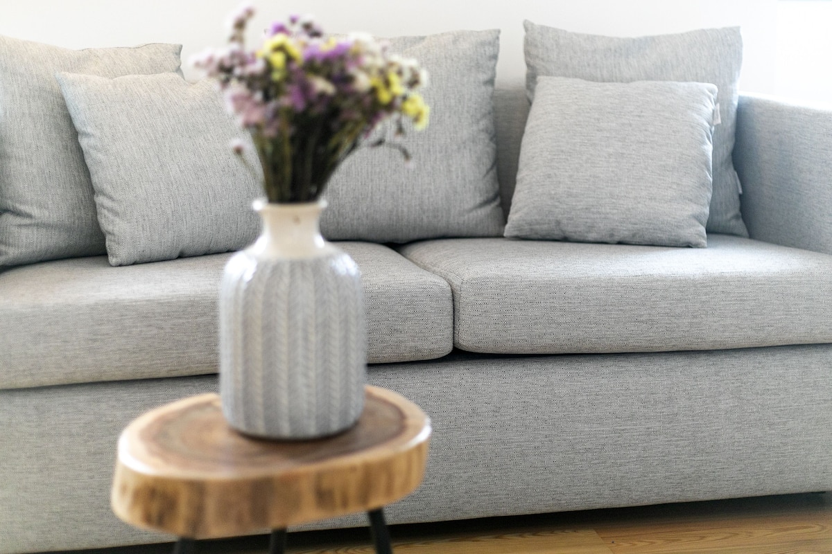 Un sofá gris con un jarrón de flores sobre una mesita de madera.