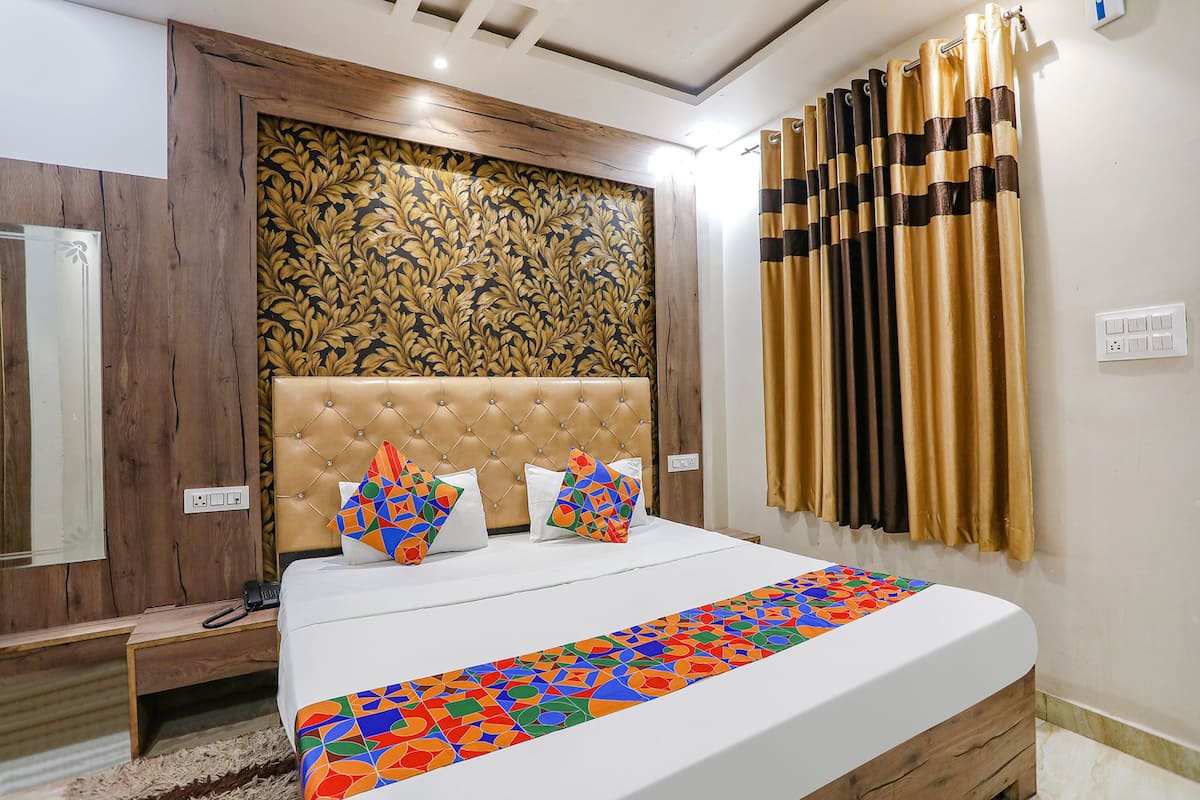 A bedroom with a tufted headboard, a patterned wall, a bed with colorful pillows, and curtains.