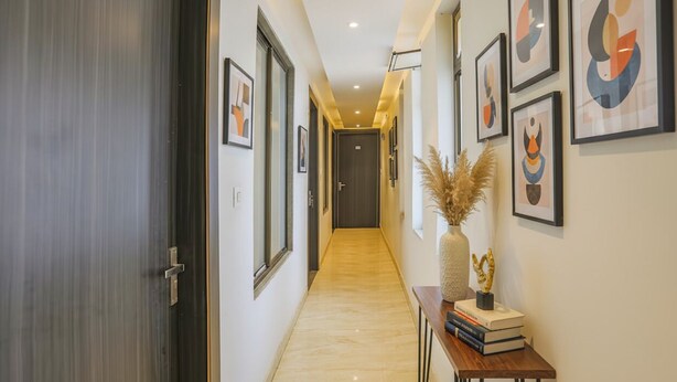 A hallway with framed artwork on the walls, a door labeled "201", and a console table with books and a vase. - FabHotel Shri Ram Kashi (Prayagraj)