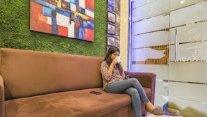 A person sitting on a brown sofa in a lobby area with a green wall and a colorful abstract painting. - FabHotel Shri Ram Kashi (Prayagraj)