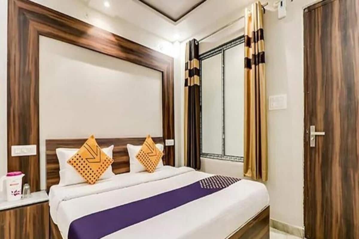 A hotel room with a large bed, wooden headboard, curtains, and a window.