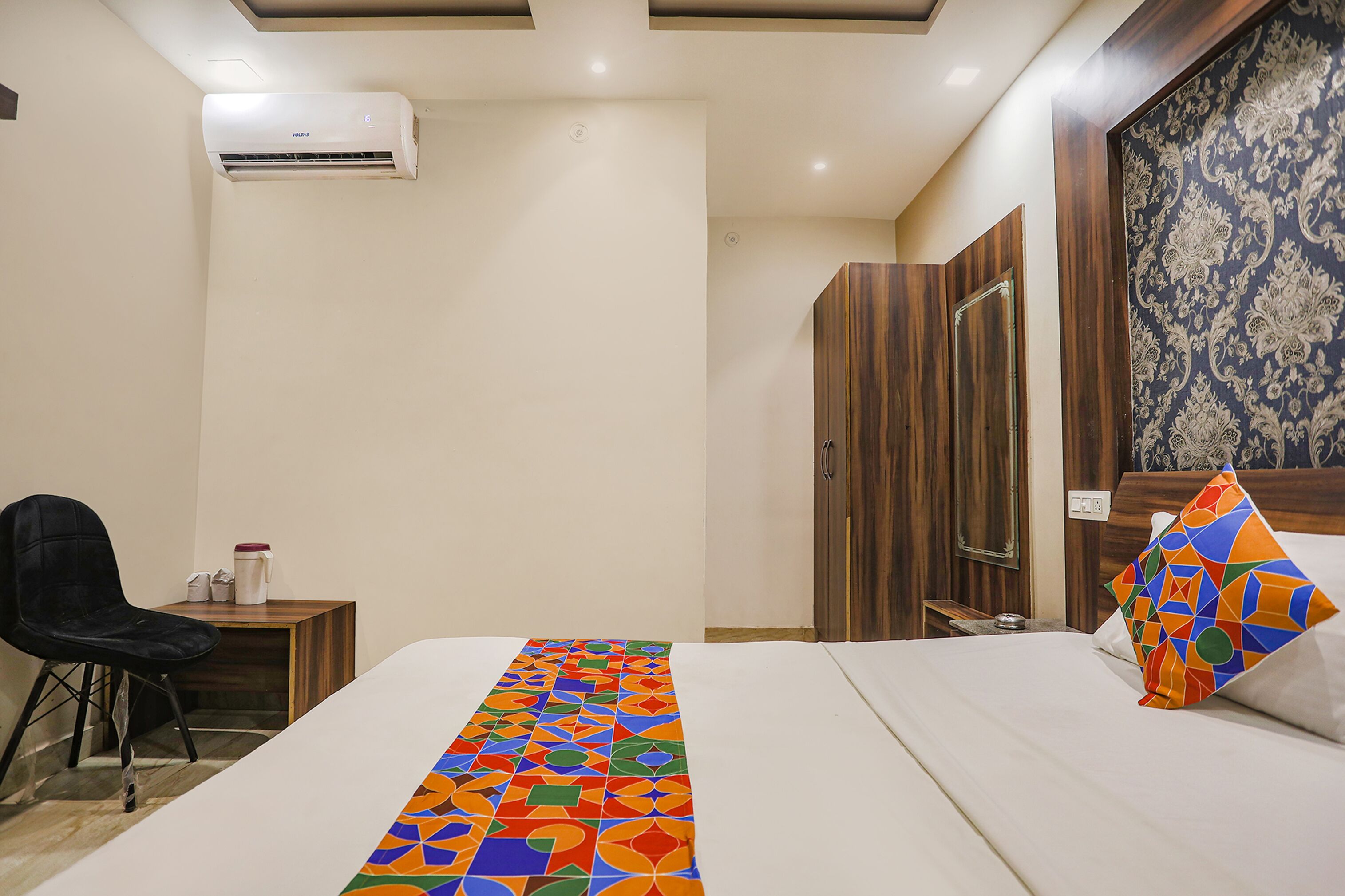 Habitación de hotel con cama, una silla, mesita de noche, armario y aire acondicionado.