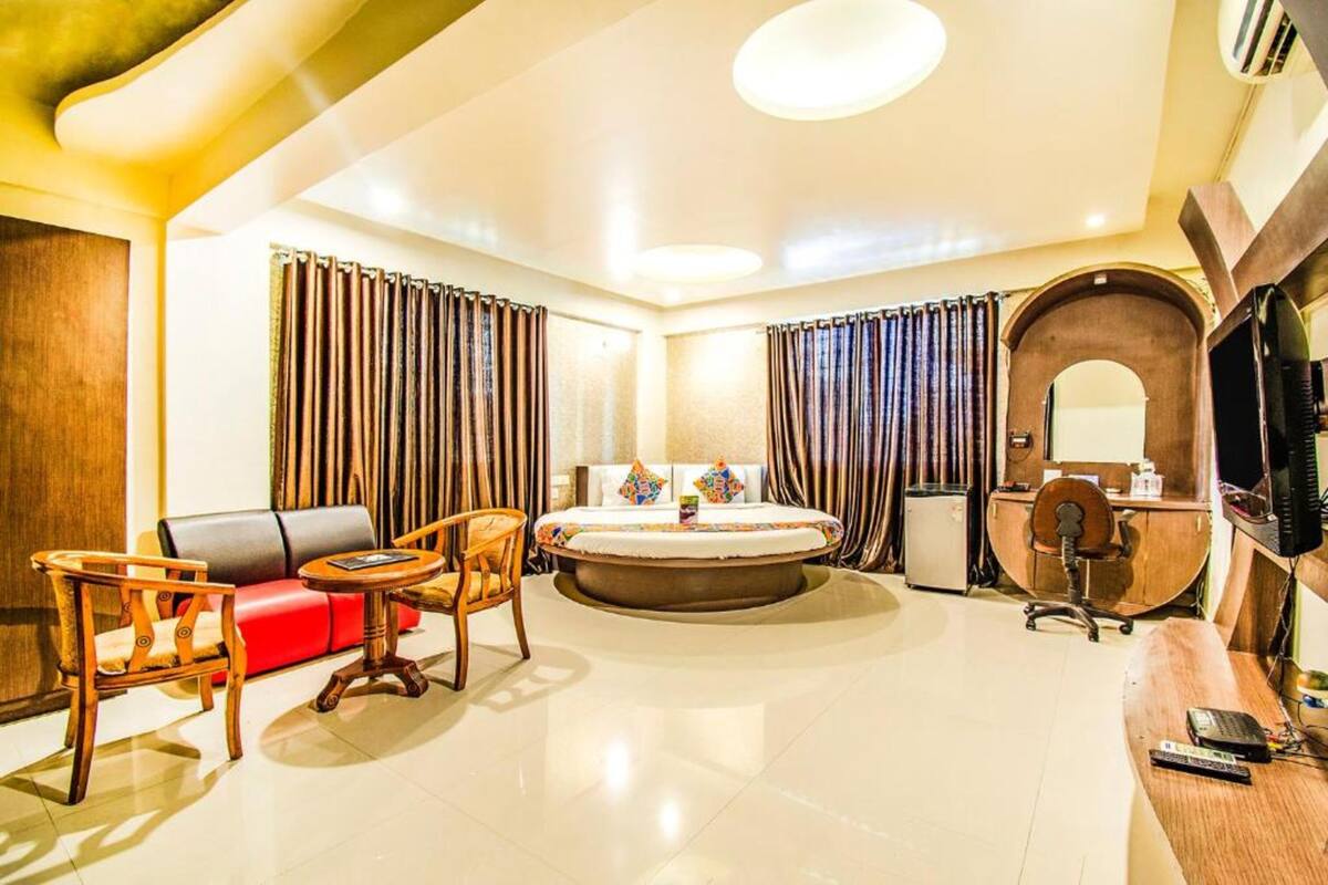 A modern hotel room with a round bed, a desk, a chair, a sofa, and curtains.
