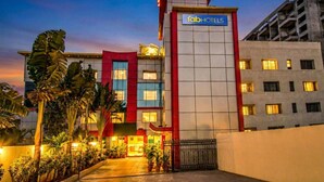 Un hôtel à plusieurs étages, reconnaissable à son grand panneau « Fab Hotels », à sa façade rouge et blanche et à son entrée fermée par un portail, agrémentée de plantes en pot.