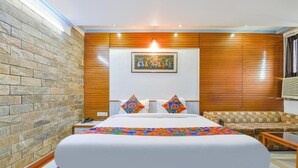 A bedroom with a large bed, a wooden headboard, a stone wall, a colorful artwork, and a sofa. - FabHotel Fly view (Jaipur)