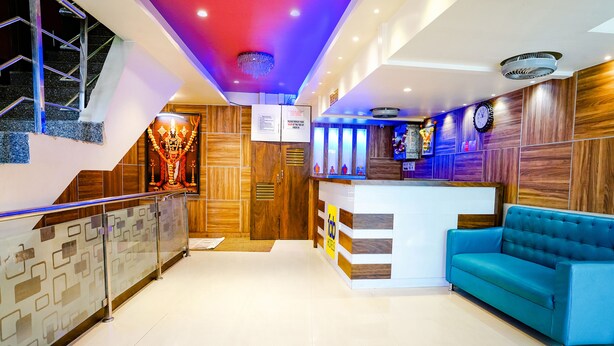 Un hall de hotel con una recepción, un sofá azul, una escalera y una pared decorativa con un reloj.