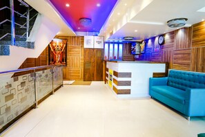 A hotel lobby with a reception desk, a blue sofa, a staircase, and a decorative wall with a clock. - Fabhotel Kwality Inn (Mumbai)