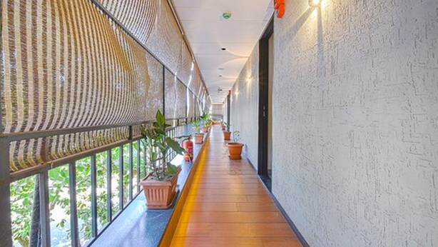 A corridor with a wooden floor, potted plants, and a patterned ceiling. - Fabhotel Udhna Inn (Surat)