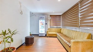 A modern waiting area with a sofa, a small table, a potted plant, and a vending machine. - Fabhotel Udhna Inn (Surat)
