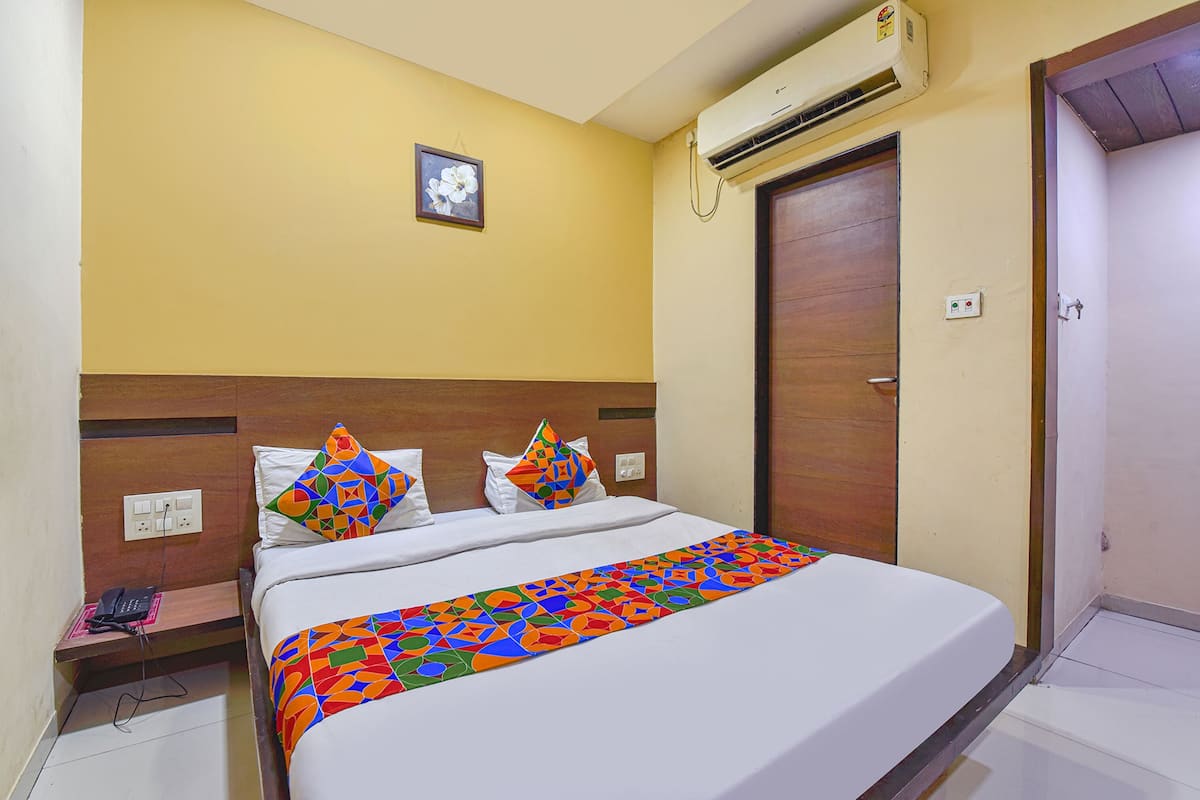 Habitación de hotel con cama, unidad de aire acondicionado, una puerta y toma de corriente.