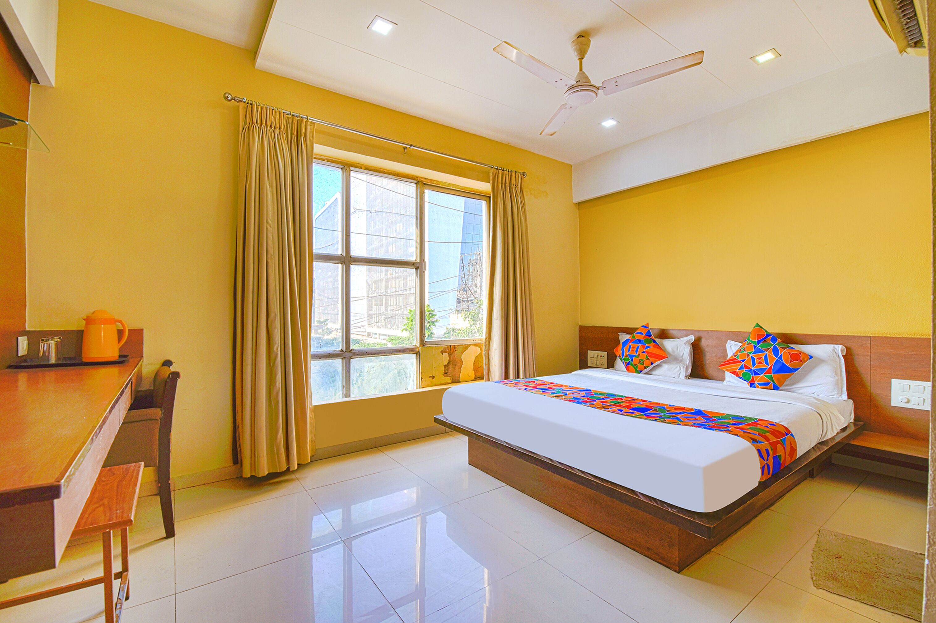 A hotel room with a large bed, a desk, and a window with curtains.