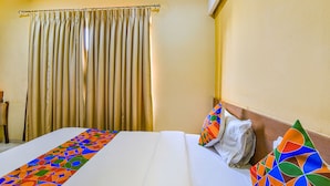 A hotel room with a large bed, a curtain, and a colorful pillow. - Fabhotel Rb Residency (Surat)