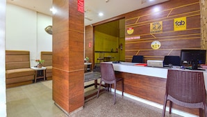 A hotel reception area with a wooden reception desk, two wicker chairs, a sofa, and a small table with a vase. - Fabhotel Rb Residency (Surat)