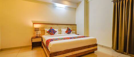 A neatly made bed with a wooden frame and a colorful quilt, a bedside table with a lamp, and a window with curtains.
