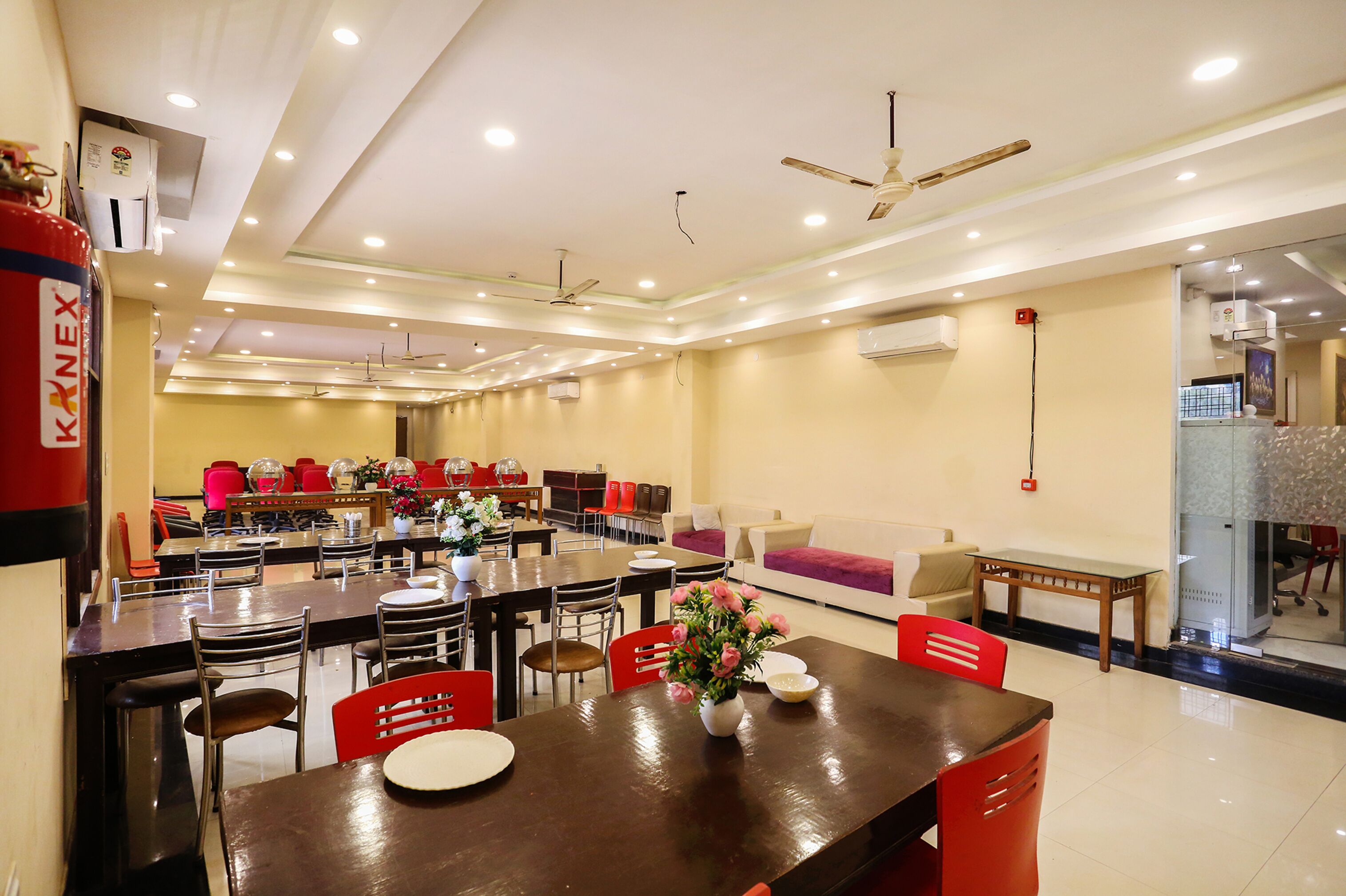 A spacious dining area with multiple tables and chairs, ceiling fans, and an air conditioning unit.