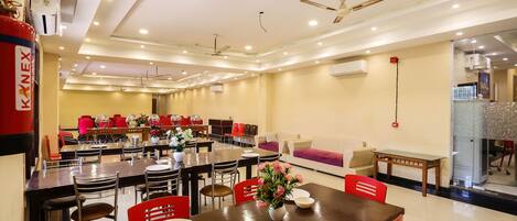 A spacious dining area with multiple tables and chairs, ceiling fans, and an air conditioning unit.