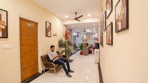 A hotel lobby with a reception desk, a seated guest, and a wooden door marked with the number 113. - FabHotel GK Residency (New Delhi)