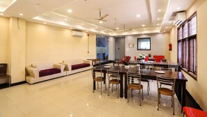 A modern dining area with a long table, chairs, and a sofa. - FabHotel GK Residency (New Delhi)