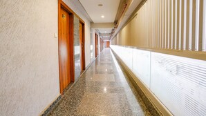 A long, polished corridor with wooden doors and a glass wall on one side. - Fabhotel La Victoria (Surat)