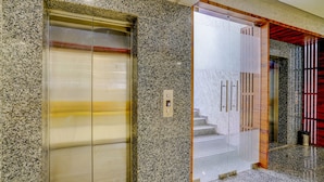 An elevator with a digital display, a glass door, and a staircase leading to a red door. - Fabhotel La Victoria (Surat)
