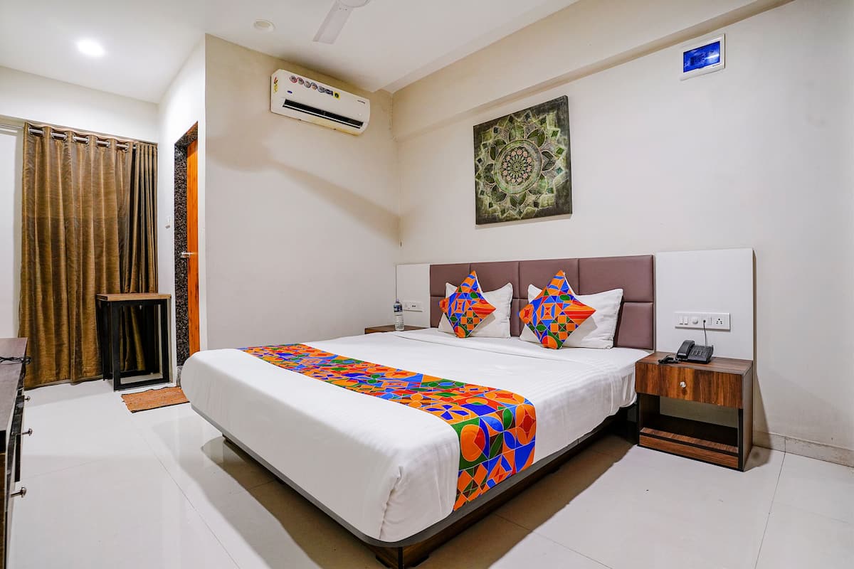 A hotel room with a bed, a nightstand, an air conditioner, a wall-mounted artwork, and a door.