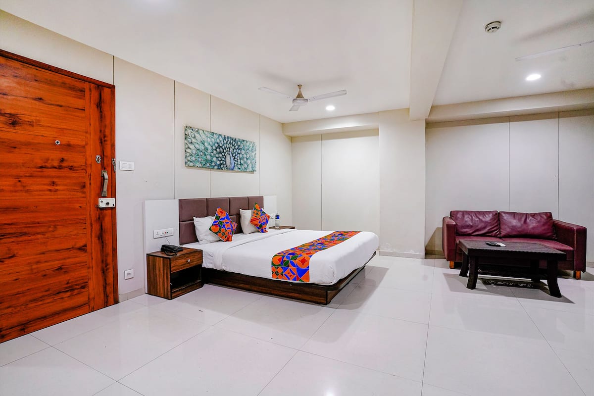 A bedroom with a bed, bedside table, nightstand, and a red leather sofa.