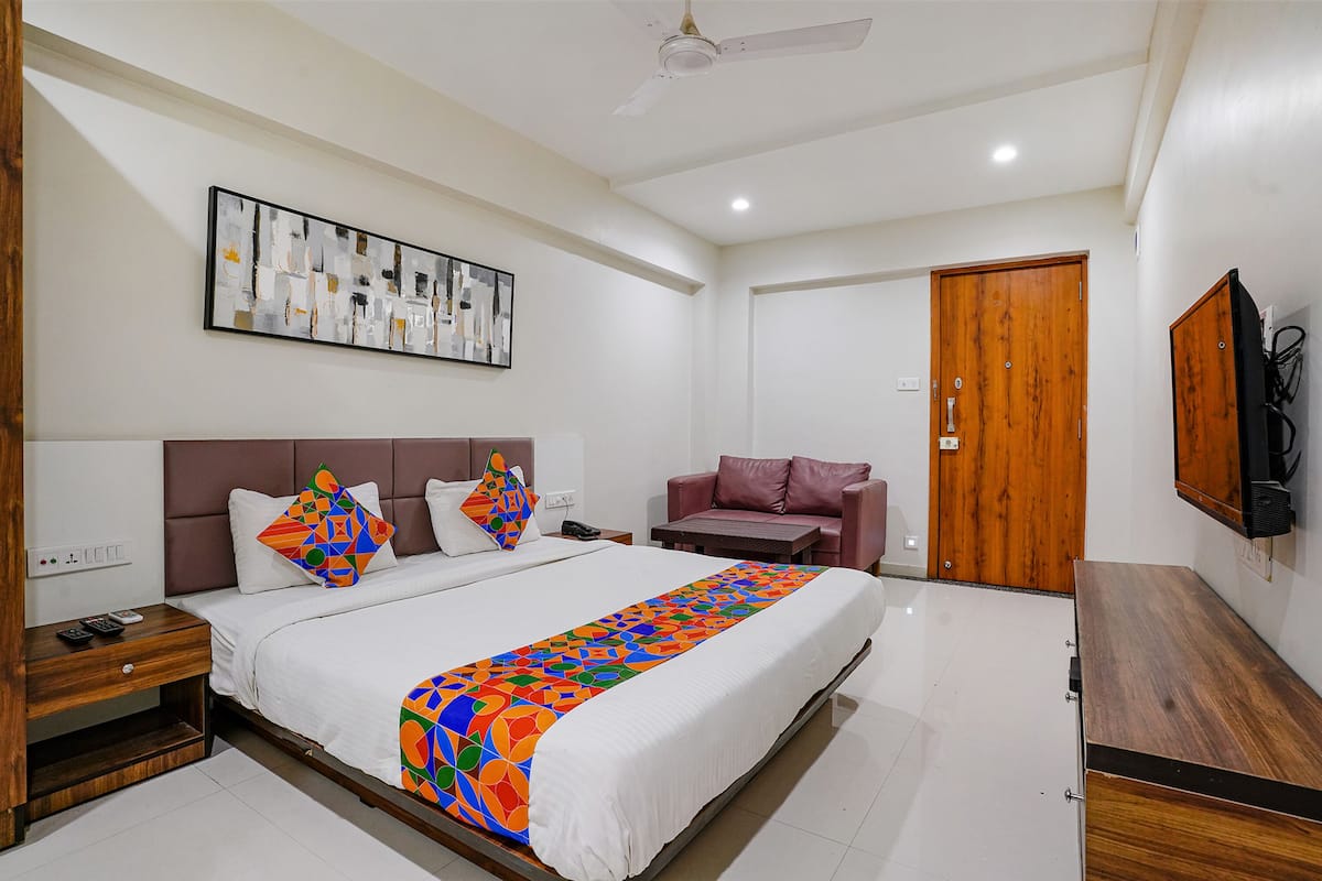 A hotel room with a bed, a sofa, a TV, and a wooden door.